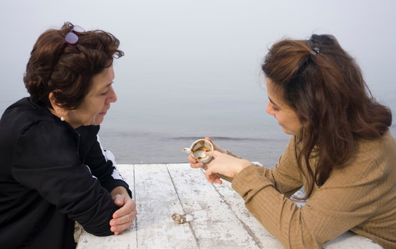 Fortune telling and traditional turkish coffee concept on coast. Woman telling fortune to elder woman by inspecting the brown grounds remaining in coffee cup. Young woman guessing on coffee grounds.