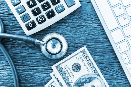 Top view dotor workspace. The stethoscope on wooden table with note book and calulator with money for dotor fee