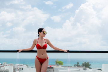 Happy woman beside a rooftop pool with a beautiful city and ocean view on background