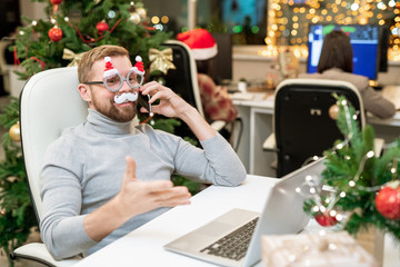 Happy businessman in xmas eyewear congratulating business partners on the phone