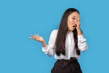 Freestyle. Young woman wearing shirt and skirt standing isolated on blue showing copy space aside covering face shocked