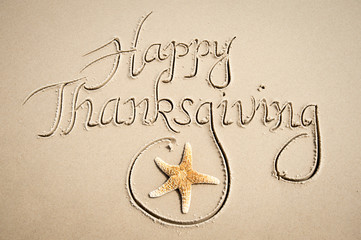 Happy Thanksgiving message handwritten in calligraphic script on smooth sand beach with decorative starfish flourish