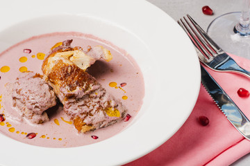 Close up of grilled chicken breast under pomegranate and walnut sauce on white plate on light stone background