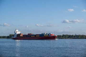 A cargo ship sailing on a navigable river on a sunny day. The container ship is on the route.
