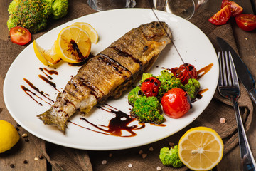 Grilled fish with roasted vegetables on the white plate, served with lemon
