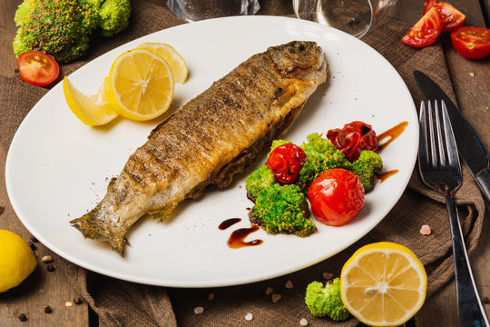 Grilled fish with roasted vegetables on the white plate, served with lemon