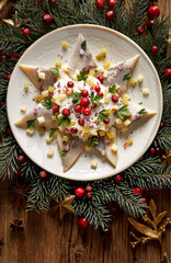 Fototapeta na wymiar Christmas Herrings fillets with cream sauce with apple, pickled cucumbers, red onion and spices, garnished with cranberries on a ceramic plate on a festive decorated wooden table, top view
