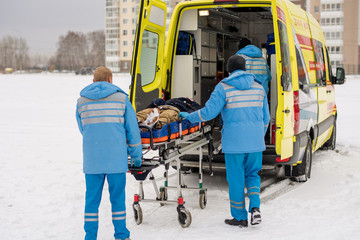 Paramedics pushing stretcher with fixed unconscious man into ambulance car