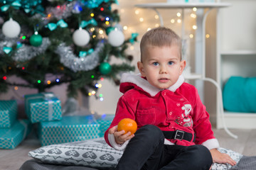 Fototapeta na wymiar Little boy with mandarine in his hands in Christmas decorated interior