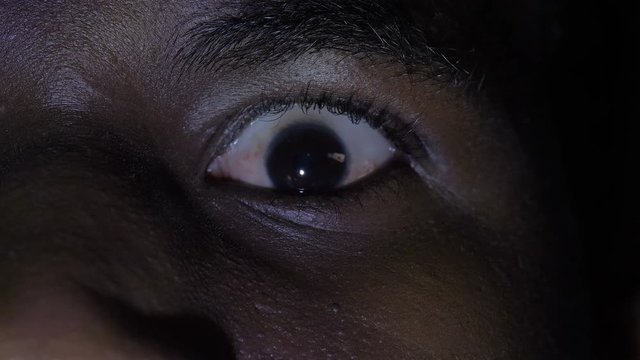 scared, scary black man opening his eye in the dark. Danger, fear