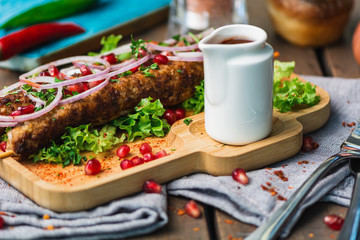 Shish kebab on a stick, from ground beef meat. Lula kebab, traditional Caucasian dish. On the wooden background of the concrete, on a chopping board, with satsebeli, spices and tomatoes