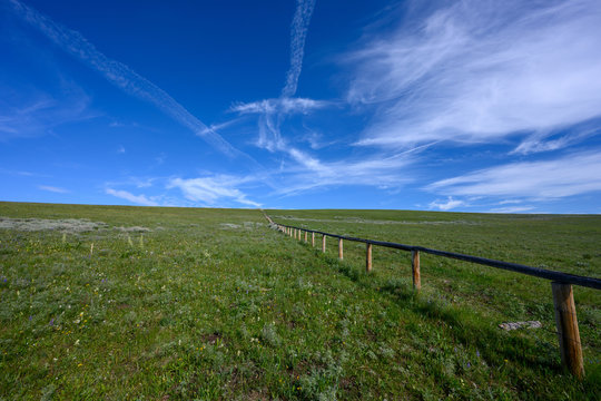 Blue Sky and Clouds Over Green Field with Wooden Fence