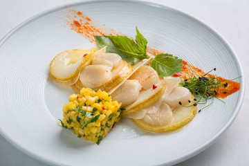 Scallop slices with pear and mango on a white plate.