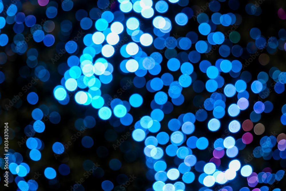 Wall mural illuminated abstract round bright blue bokeh on dark background. colourful glitter bokeh from out of