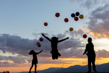 Silhouette happy family playing with colorful balloons on mountain park at summer sunset, summer holidays concept