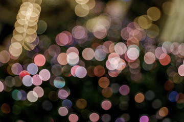 Illuminated abstract round pink, yellow purple and gold bokeh on dark background. Colourful glitter bokeh from out of focus view of decoration bulbs.