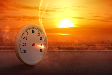 The thermometer on the street with a high temperature on the city with a glowing sun background