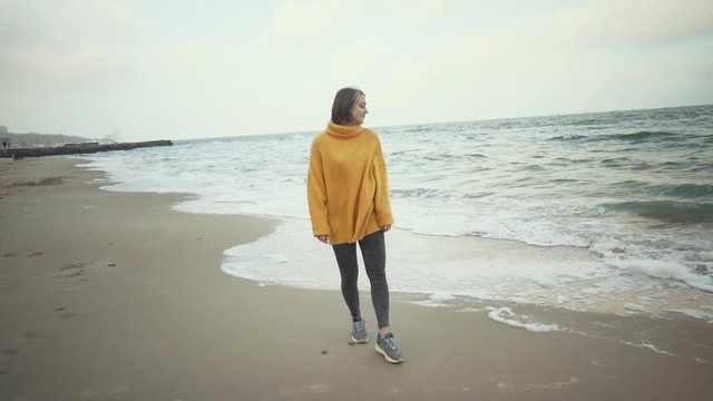 Young beautiful woman in orange sweater walking on the beach in cold weather