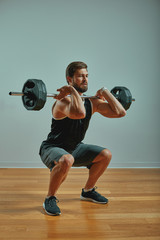 Portrait of super fit muscular young man working out in gym with barbell on gray background,...