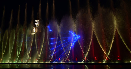 Colorful water fountains. Beautiful laser and fountain show. Large multi colored decorative dancing water jet led light fountain show at night. Dark background.