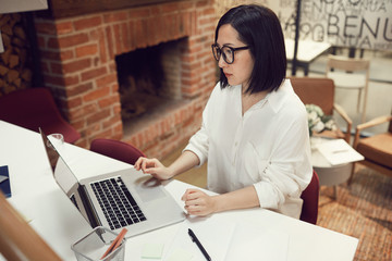 High angle portrait of contemporary Asian woman using laptop while working in business office, copy space