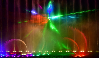 Colorful water fountains. Beautiful laser and fountain show. Large multi colored decorative dancing water jet led light fountain show at night. Dark background.