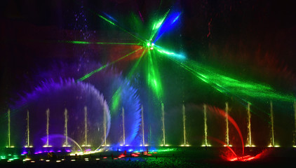 Colorful water fountains. Beautiful laser and fountain show. Large multi colored decorative dancing water jet led light fountain show at night. Dark background.