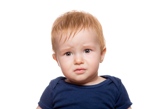 Portrait Of A Boy With A Frustrated Face And Frowning Eyebrows, Todler With Red Hair And A Blue Bodysuit Isolated On A White Background.