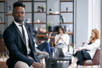 Good-looking african man wearing black suit stand posing in modern office and look at camera....