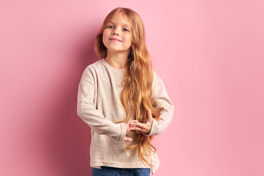 Beautiful girl of caucasian appearance with golden long hair, big beautiful charming eyes, wearing white blouse look at camera isolated on pink background. Children concept