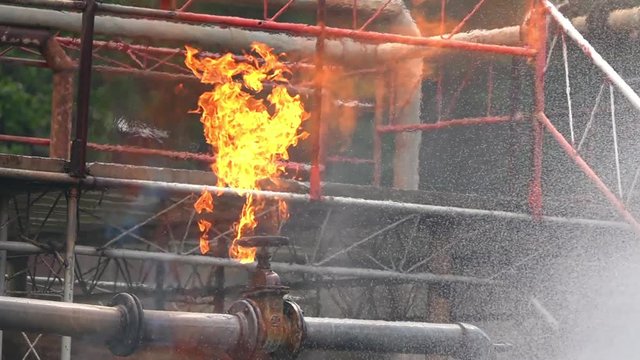 HD Slow motion of firefighter on safety rescue duty using water extinguisher spraying water from a hose extinguishing to control crackle fire flames from gas pipeline leaking. Fireman fighting a fire.