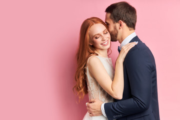 Attractive woman with auburn hair hugging her fiance in elegant suit kissing her. Happy young family, love concept