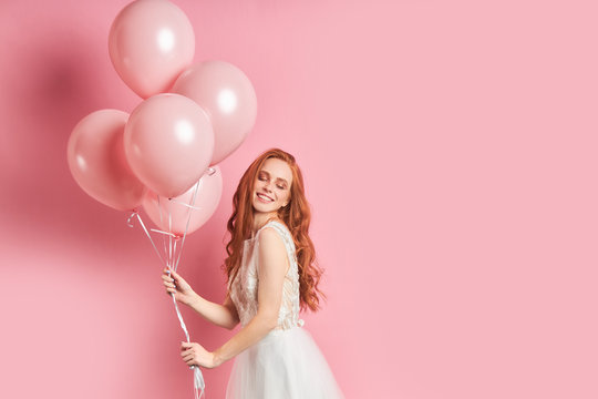 Cute young caucasian woman holding a lot of pink air balloons isolated over pink background. Smile, happy