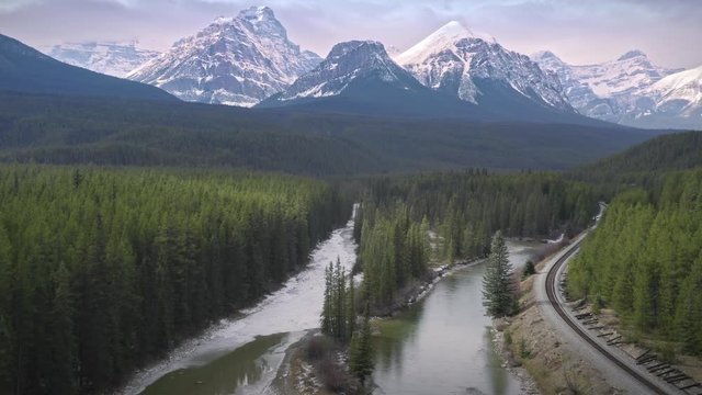 Aerial: Train tracks forest & river at Morant's Curve near Lake Louise in The Canadian Rocky Mountains. Alberta, Canada.
