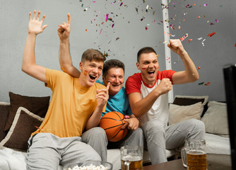 Father and two sons celebrating after basketball match win on TV, confetti falling from air 