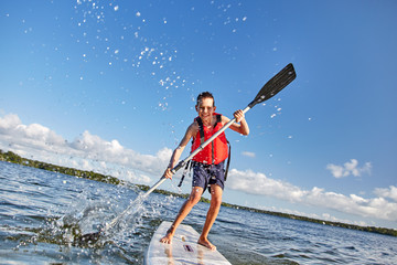 happy boy paddling on stand up paddleboard. cheerful child having fun on water. Summer vacation...