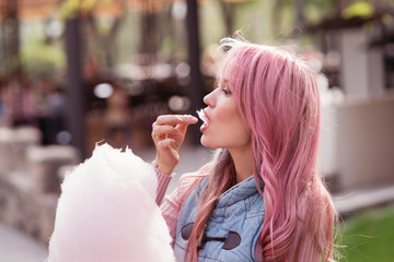 Adorable young woman with long pink hair eats and poses with sugar pink candy cotton. Concept happy...