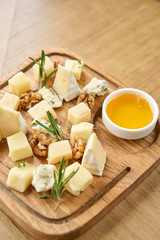 Cheese plate. Delicious cheese mix with walnuts, honey on wooden table. Tasting dish on a wooden plate. Food for wine.