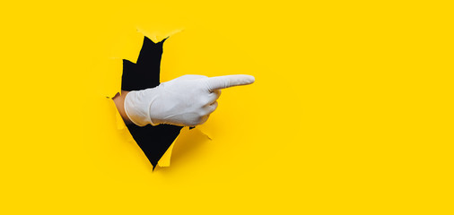 The forefinger points in white medical glove to the right side. Yellow paper background with torn...