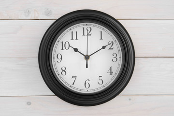 wall round clock black with white color and number classic or clockwise with 10 o'clock 10 minutes by short needle pointing ten digits and long needle pointing number two on vintage white wooden wall