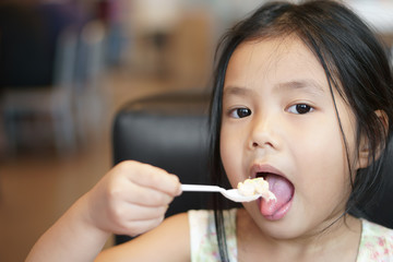 Asian child cute or kid girl enjoy eating tuna salad and corn vegetable with yogurt for delicious breakfast and healthy food in morning with holding plastic spoon at home or restaurant and coffee shop