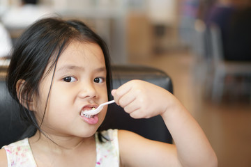 Asian child cute appetite or kid girl enjoy eating tuna salad and corn vegetable or yogurt for breakfast and healthy food in morning with holding plastic spoon by left hand at home or cafe restaurant