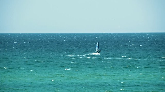 View of the man on a windsurf catching the wind on sea water against the blue clear sky. Shot. Summer resort
