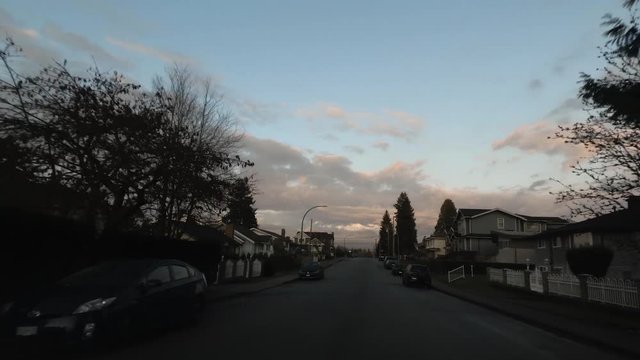 view from car windshield that ride on the road to the outskirts of the city between one-story private houses, a pink sky with clouds glows in the background