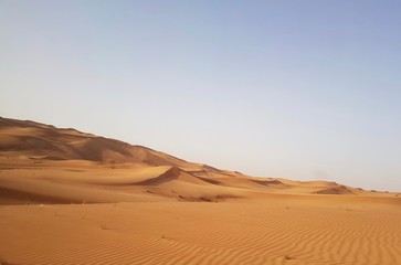 Fototapeta na wymiar Landscape of desert in Dubai, sand dunes which lack of water and vegetation in hot weather under the blue sky in daylight and rapid temperature change between day and night when darkness revisited