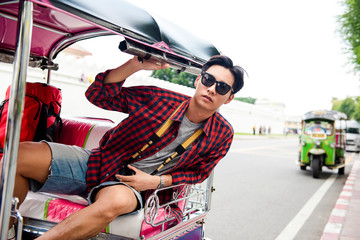 Asian tourist man riding TukTuk taxi while traveling in Bangkok Thailand