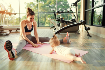 Parenthood and sport lifestyle. Young mother doing yoga with baby girl in gym.