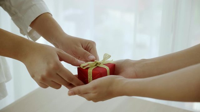 Close up at hand is sending small red gift box tied to golden bow handed to the people. Giving gifts during the Christmas season, Happy New Year and Happy Birthday. Concept of online delivery business