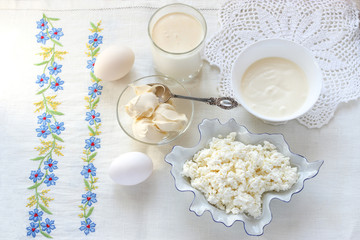 natural rustic dairy products and eggs on white embroidered tablecloth - homemade cheese, butter, cream, milk, eggs