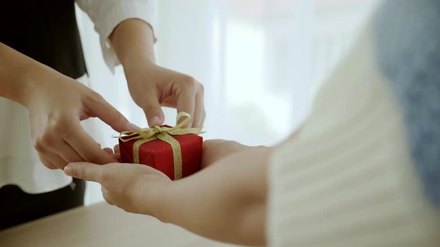 Close up at hand is sending small red gift box tied to golden bow handed to the people. Giving gifts during the Christmas season, Happy New Year and Happy Birthday. Concept of online delivery business